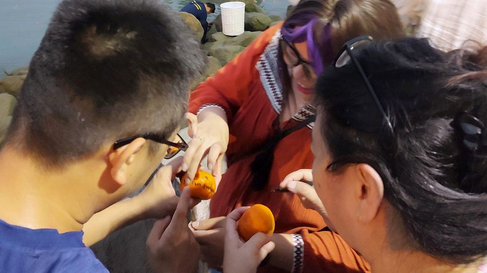People writing on mandarin oranges at the Esplanade sea wall before tossing them into the sea
