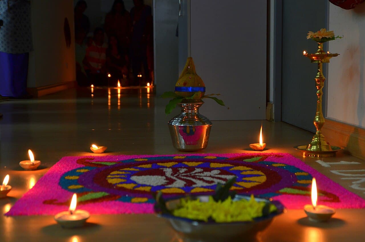 A bright Deepavali kolam pattern on the floor, surrounded by small lit oil lamps